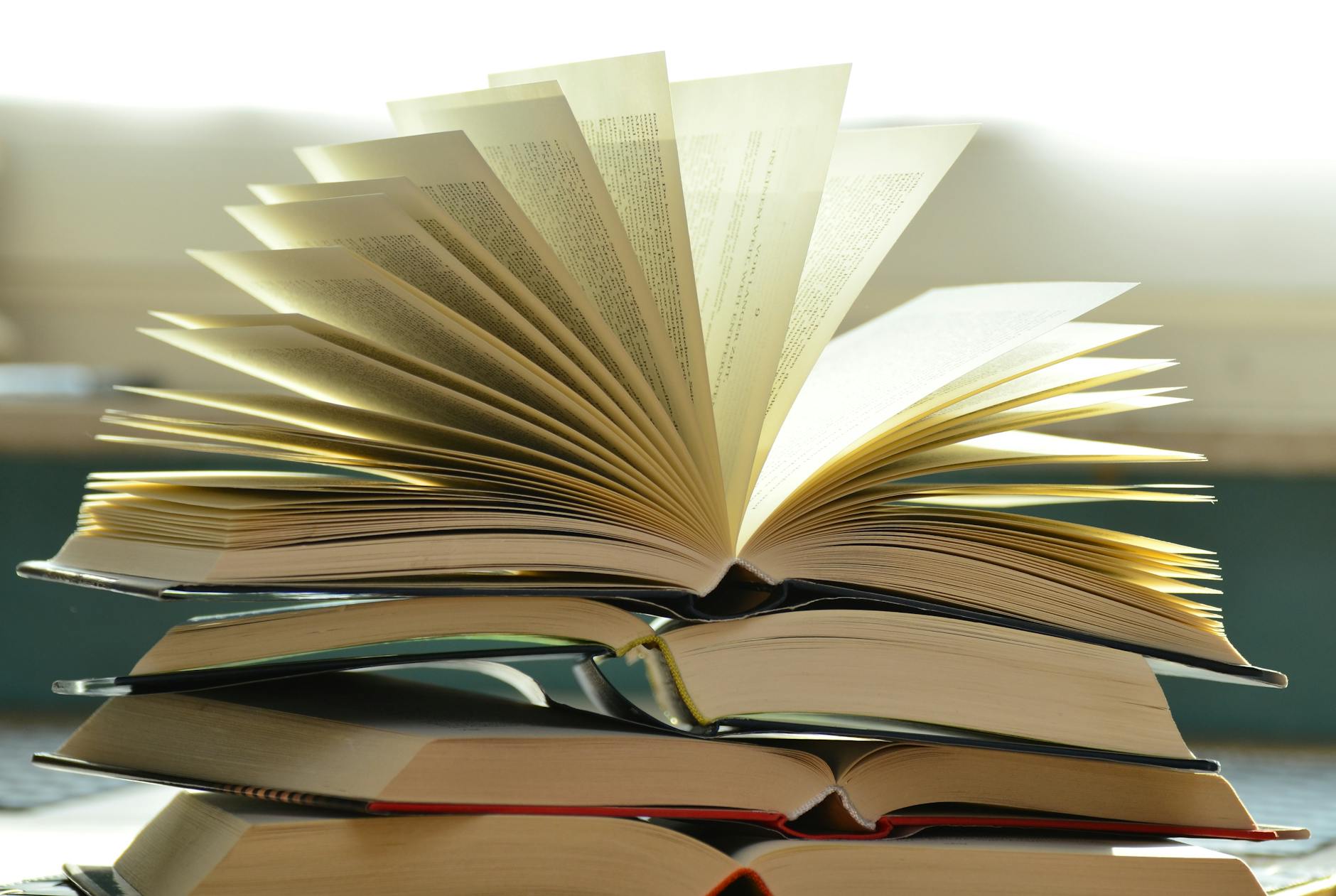 A close-up of a stack of open books with pages fanned out, capturing a study atmosphere