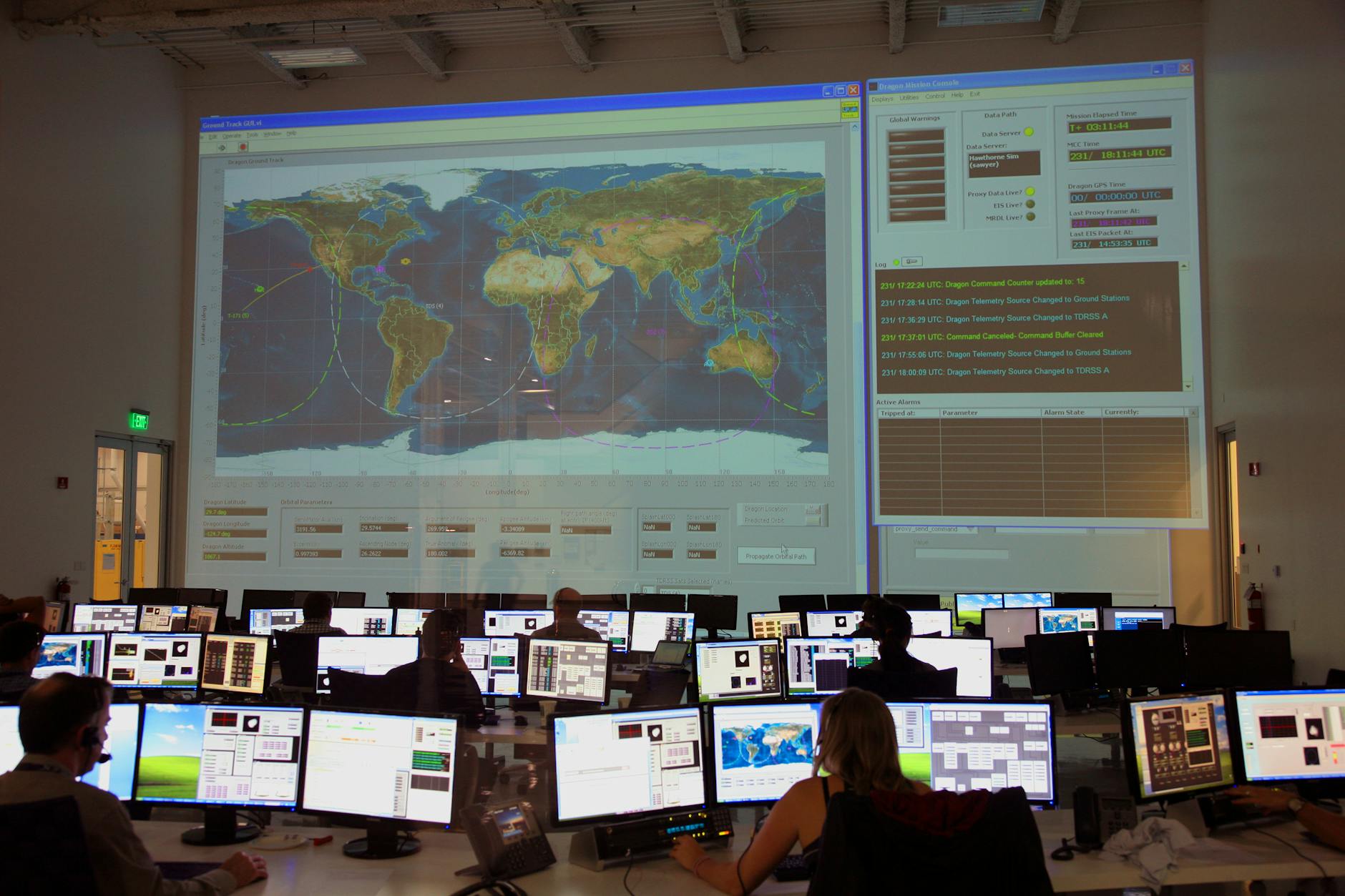 A dark security operations control room with large wall-mounted screens and analyst workstations